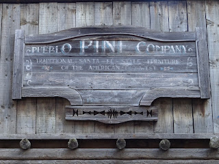 A faded sign on one of the buildings that reads - Pueblo Pine Company Traditional Santa Fe Style Furniture of the American Mid West.  Photo by Kevin Nosferatu for the Skulferatu Project.