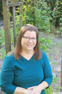 Author Erin Stevenson shown in the foreground with nature setting in the background. Erin is wearing a blue blouse.