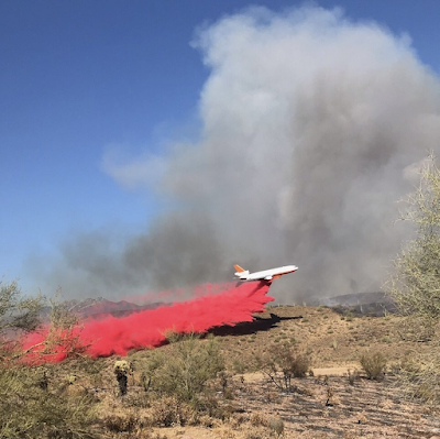 Airtanker dropping retardant in a high desert ecosystem while a firefighter looks on in the distance.