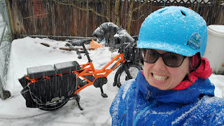 a woman standing in front of a cargobike in the snow