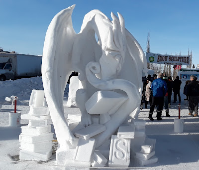 Photo of a snow sculpture of a dragon sitting among a pile of books.