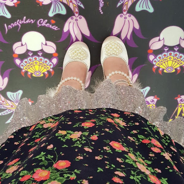 patterned Irregular Choice floor wearing floral dress with sequins trim and white Eros shoes