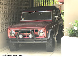 Early Ford Bronco, maroon with black soft top parked at fancy home in San Juan.