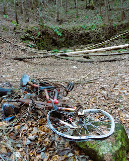 A photo of a rather battered looking abandoned bicycle lying in the woods in front of the ruins of one of the Stobsmill Gunpowder Works buildings in Gorebridge.Photo by Kevin Nosferatu for the Skulferatu Project.