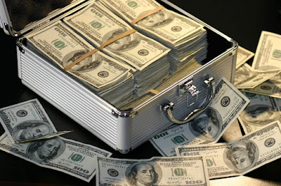 एक सूटकेस में बहुत सारे डॉलर रखे हुए हैं और कुछ नोट बाहर बिखरे हुए हैं