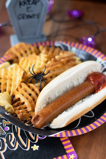 The finished Vegan Severed Finger Hot Dog on a plate with waffle fries and some Halloween decor.