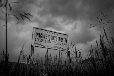 black and white photo of a sign near Red Lodge, Montana that says "welcome to God Country..Home of Carbond Counry Republicans"  Cdrefit  Ashley Gilbertson