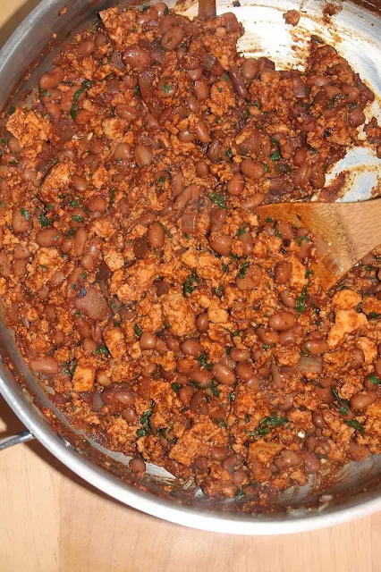 Spoon stirring a pan of spicy tofu and pinto beans.