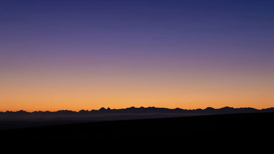 A 4K wallpaper capturing the striking silhouette of distant mountains under the gradient hues of a twilight sky.
