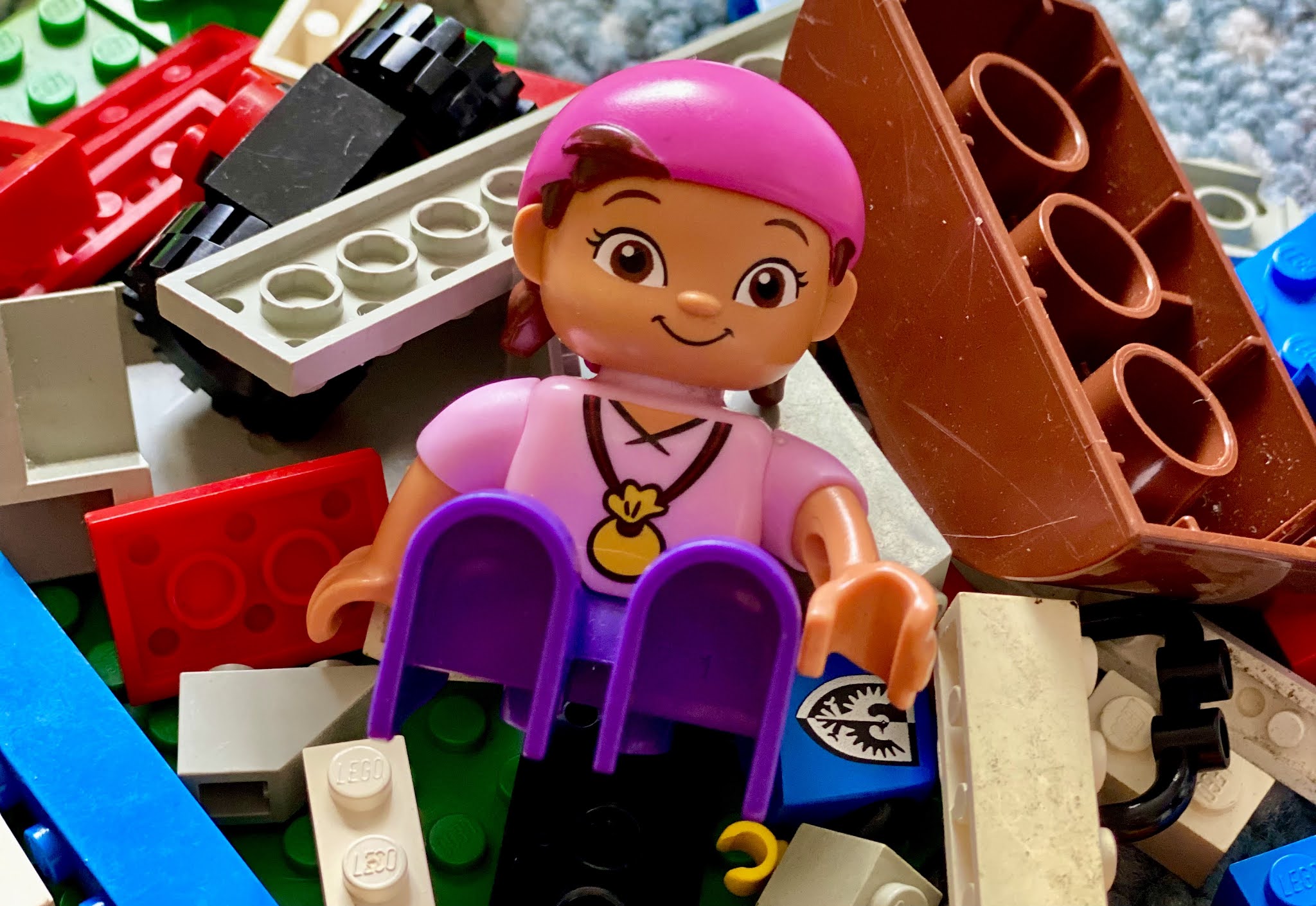 A pile of LEGO and DUPLO on a rug with a character sitting on top of it