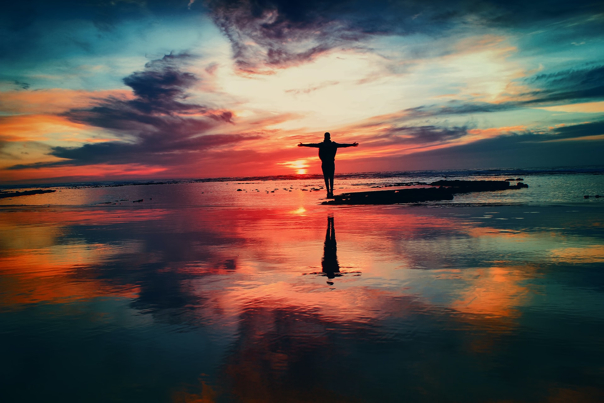 The image contains a man standing and sunset and sea in the background