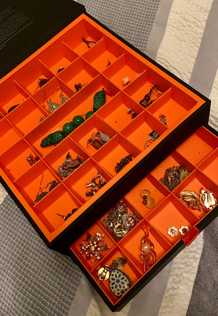 A black box with an orange lining. Inside it's split into little square cells, and there's a pair of earrings in each cell.