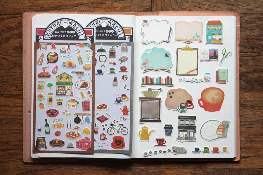 Photograph of two sheet stickers and a variety of flake stickers. The sheet stickers feature designs of restaurant dishes, condiments, and coffee. The flake stickers include large and small designs like clipboards, coffee grinders, and more.