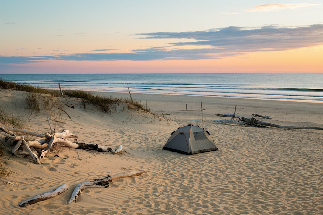 Idyllic beach camping spot with tent on sandy shore at sunset