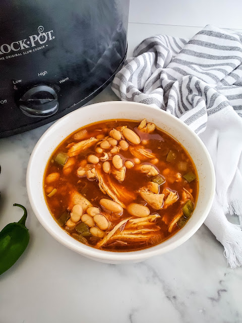 chili in a white bowl next to a slow cooker.