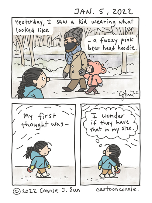 3-panel autobio comic of a girl with a braid walking in Central Park in winter. She passes a kid who is holding hands with an adult and wearing a pink bear head hoodie with a bear nose and ears, which make it look like the kid's head is in the bear's mouth. Caption reads, "Yesterday, I saw a kid wearing what looked like a fuzzy, pink bear head hoodie." In panel 2, the girl with the braid walks on. In panel 3, girl turns to look back at them. Text reads, "My first thought was -", followed by a thought bubble that says, "I wonder if they have that in my size." Original comic cartoon by Connie Sun, cartoonconnie