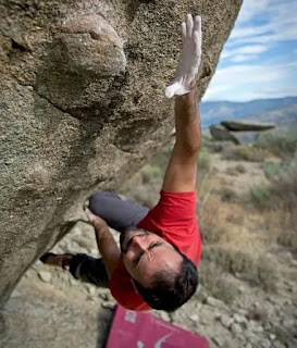 mountain climber in red t-shirt reaching out right hand to grab a ledge