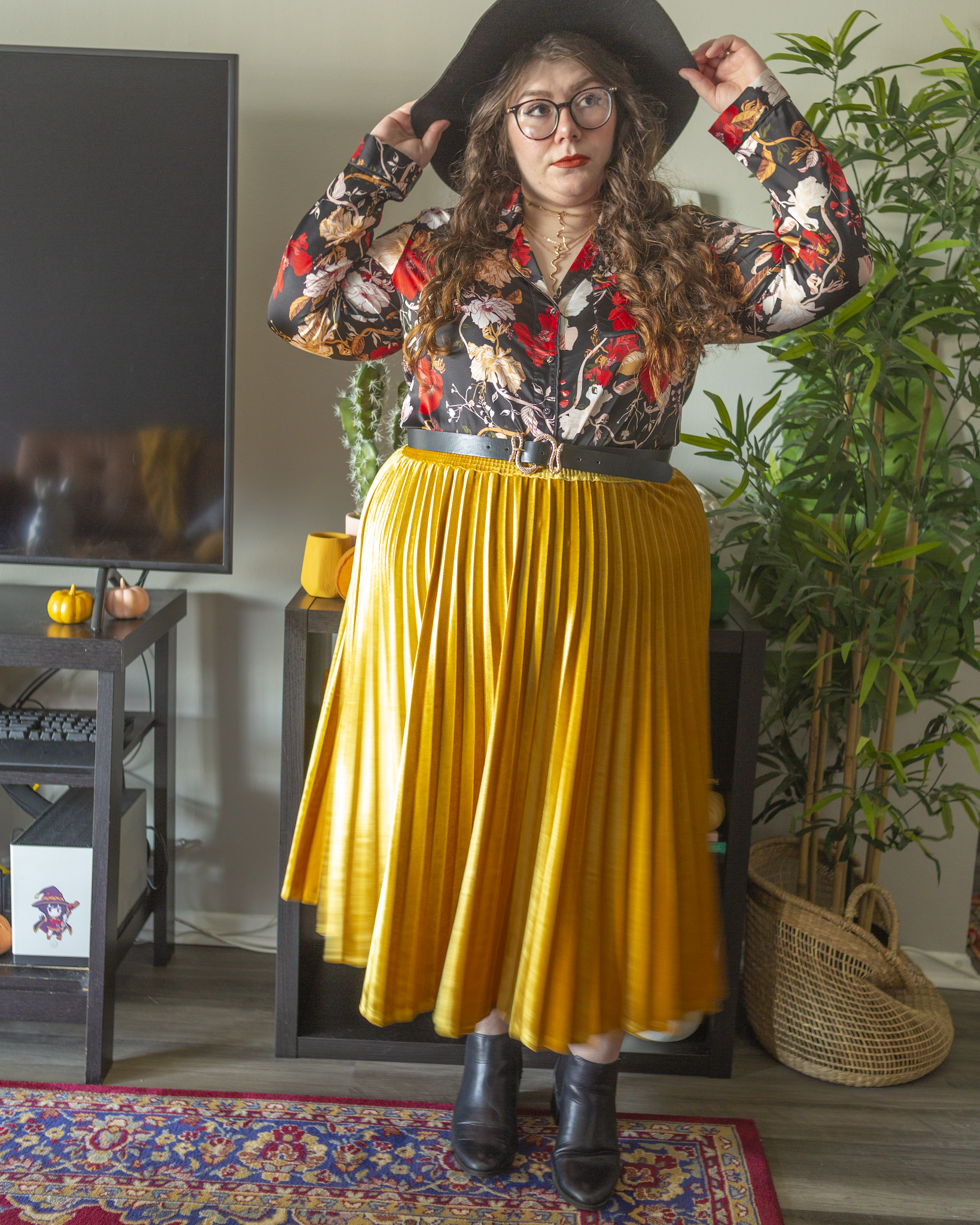 An outfit consisting of a wide brim black floppy hat, a black satin pajama style blouse with dark red, pastel pink, mustard yellow, and cream florals, tucked into a velvet mustard yellow midi skirt and black Chelsea boots.