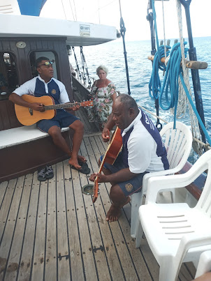 3 Fijian crew members entertaining tourists with local and classic songs while sailing .