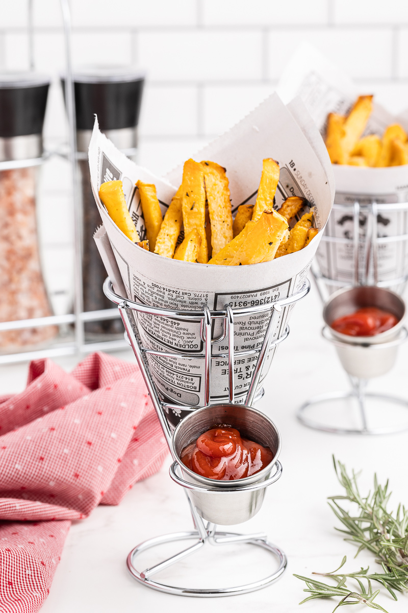 A serving of keto french fries wrapped in a newspaper cone in a metal stand.