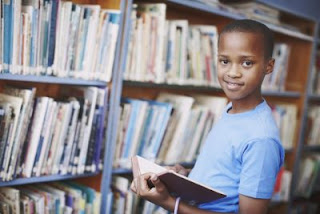 boy in front of bookshelf in a library with a children's book