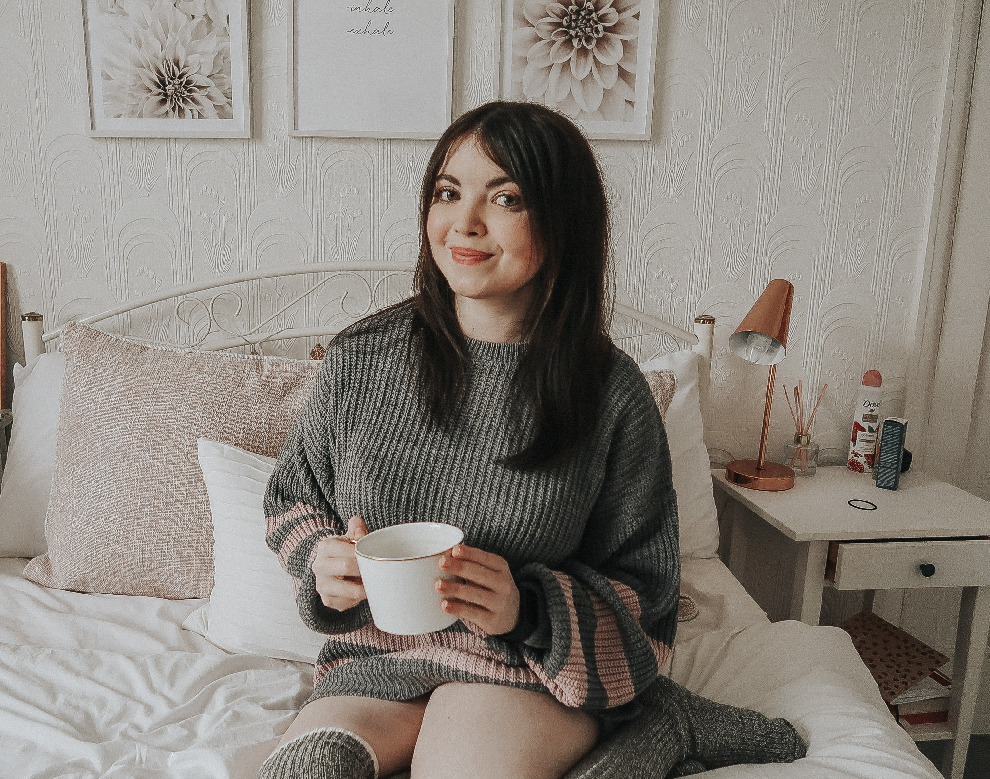 A woman in a grey and pink jumper holding a white mug.