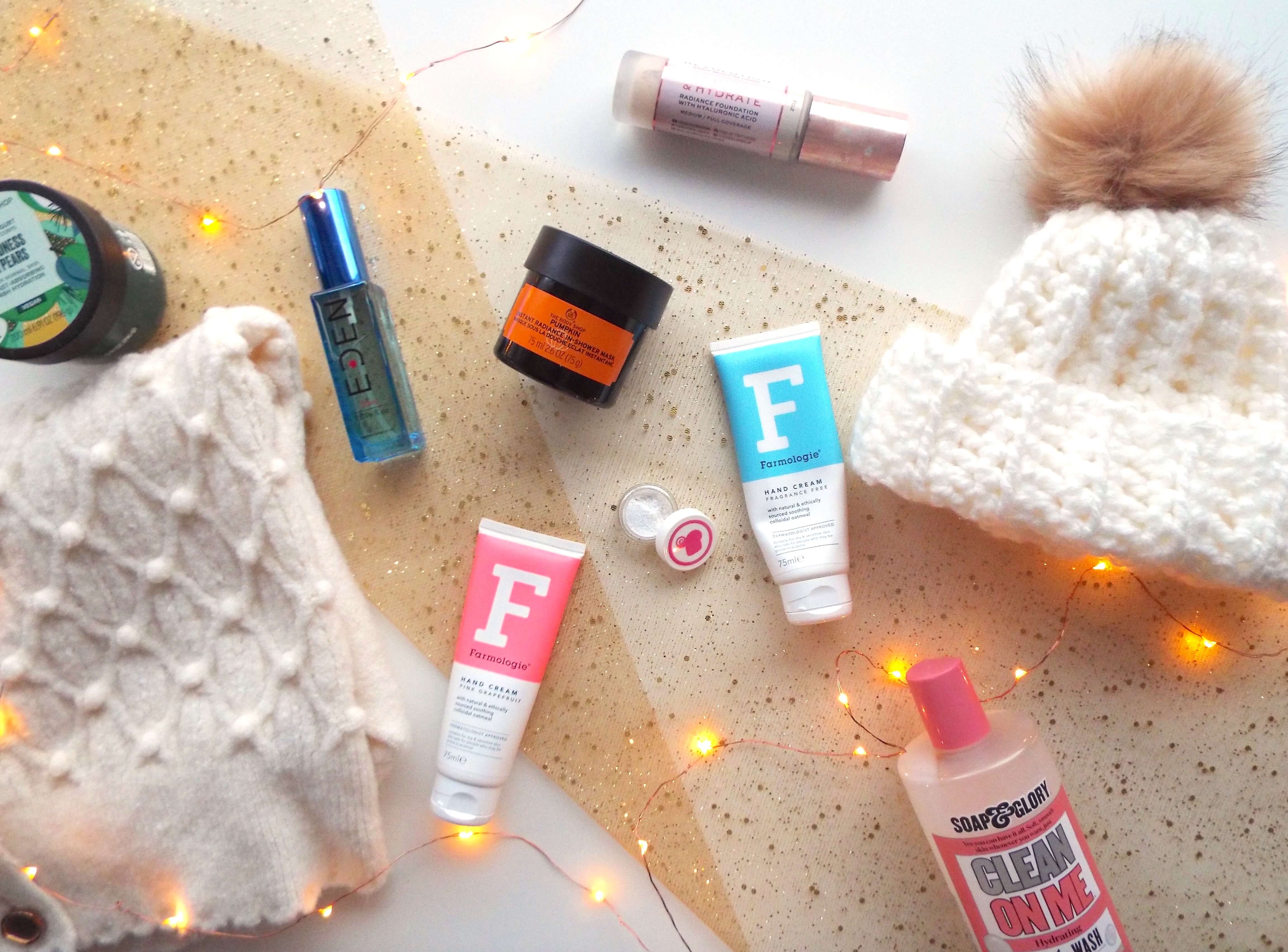 Flatlay of November and December Favourites, including an array of beauty products and a cream knit cardigan to bottom left corner, all sat on white background with gold sparkly table runner to centre.