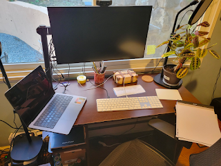 Picture of desk with monitor,  keyboard,  trackpad, and a pad of paper to the right side.  There's a window behind the monitor.