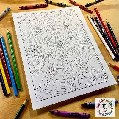 A coloring page with the phrase "Feminism Is For Everyone" rests on a wood table surrounded by Crayola art supplies.