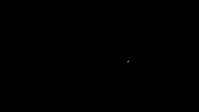 A tiny bright crescent floats in a sea of blackness.