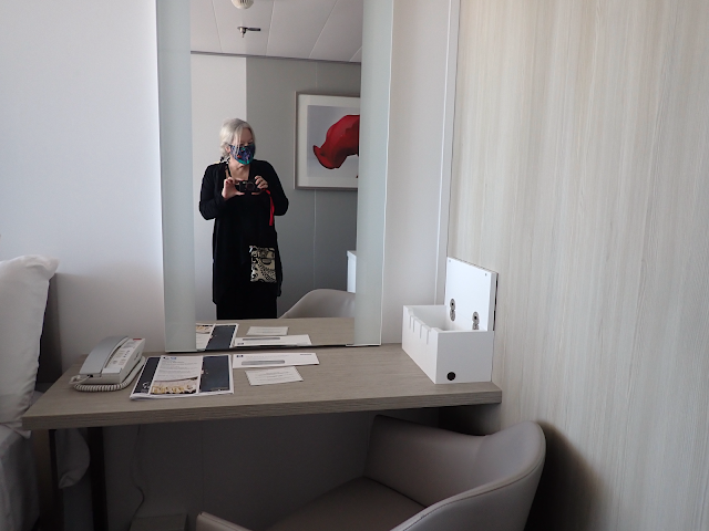 A desk with a mirror over it. A woman is reflected in the mirror taking a picture.