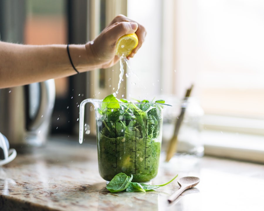 A hand squeezing lemon into a blender containing smoothie