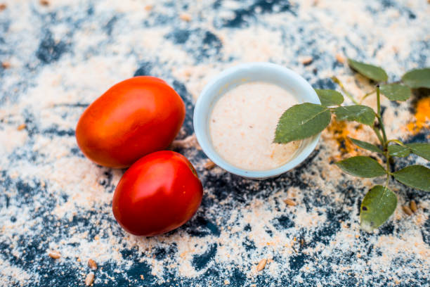 Close-up of best oil removal and ayurvedic, organic face pack of Tomato and oats with water on a wooden surface with some rose leaves and petals.