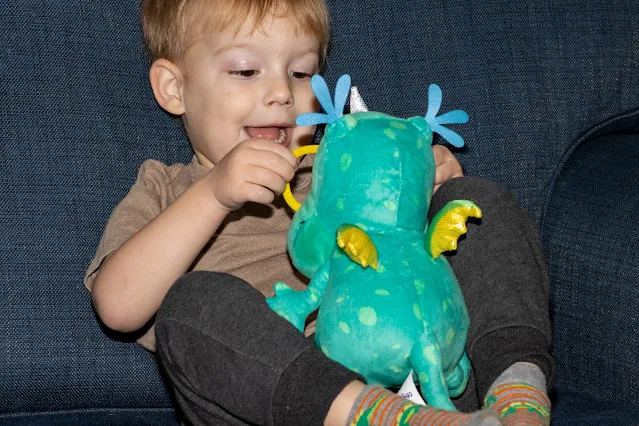 a boy pulling at the glasses on a dragon cuddly toy