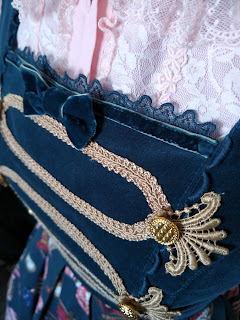 Close up of the bodice showing the velvet fabric, a bow made from velvet, lace along the square neckline and gold buttons and gold threading to create the military style look.