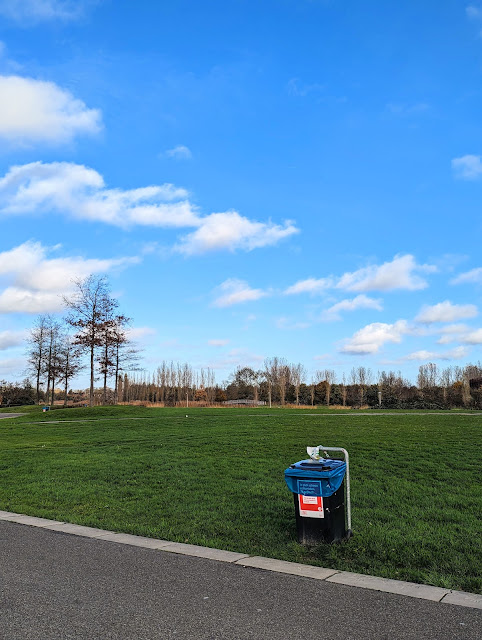 Een foto van een park met in het midden een prullenbak.