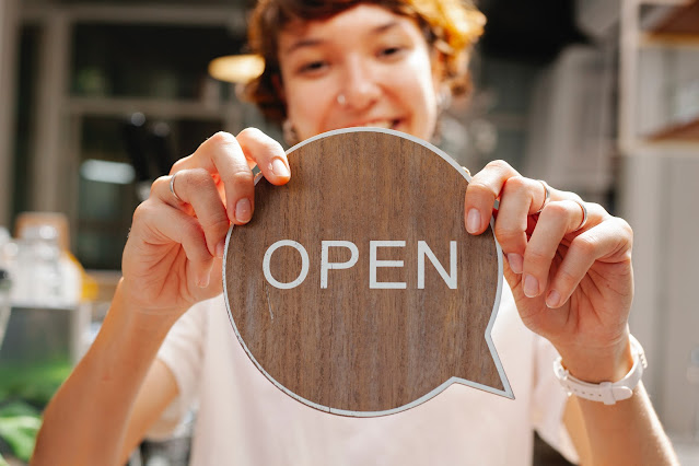 A smiling retail worker holding up an "OPEN" sign.