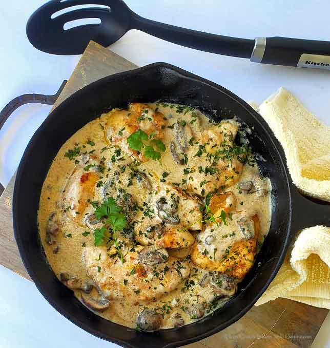 this is a cast iron skillet with a chicken in white wine sauce and bella mushrooms