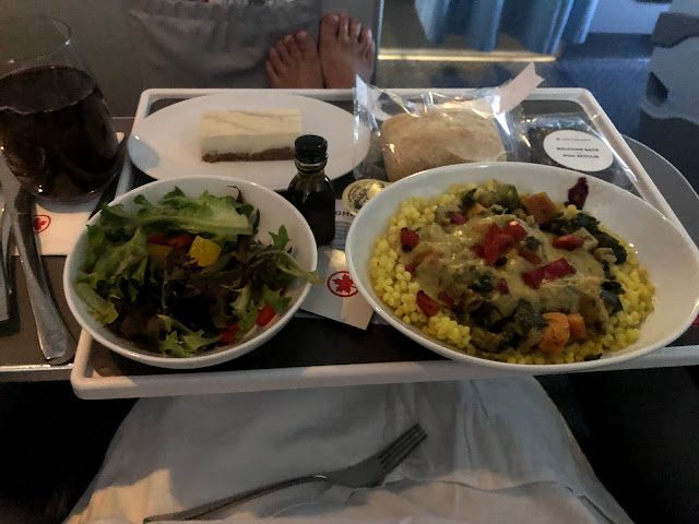 An airline meal tray containing a salad, a couscous main course, and blueberry cheesecake dessert.