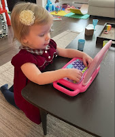 Toddler in red dress kneeling as she types on toy laptop computer