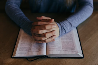 A person with prayer hands over a Bible