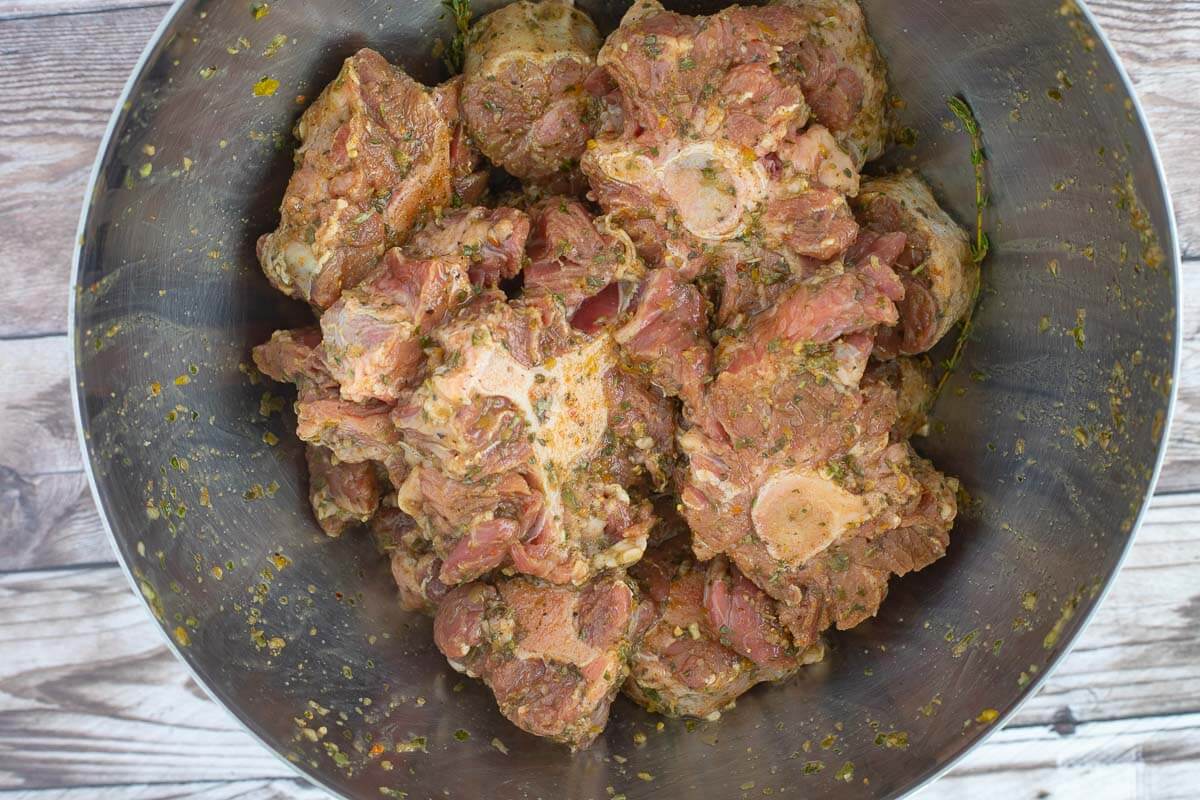 A picture of a bowl of oxtails seasoned up for stewing.