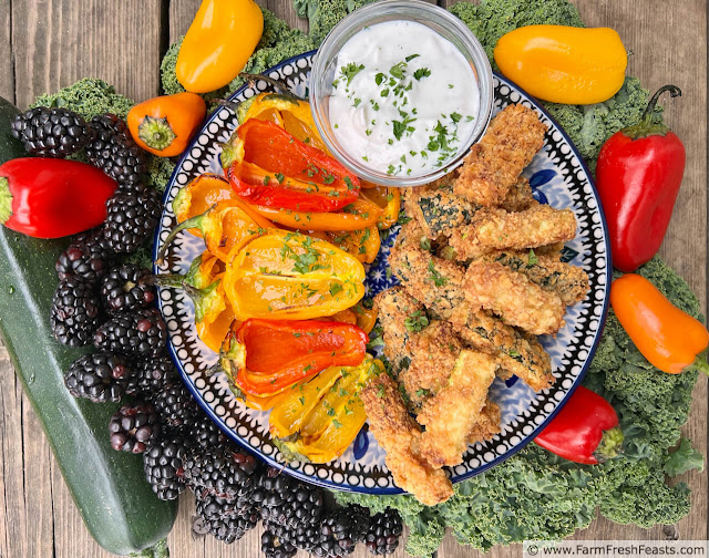 image of a plate of red and orange mini peppers and zucchini fries roasted in the air fryer, with creamy yogurt dipping sauce surrounded by fresh berries and zucchini