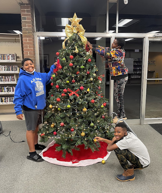 Three young boys decorate a Christmas tree at East Ensley, smiling for the camera.