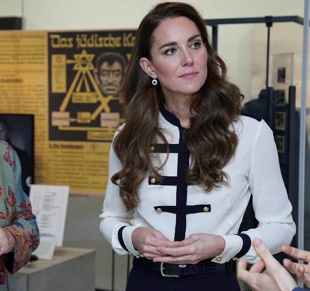 The Duchess wore a dark blue wool coat by Catherine Walker, and a white and navy military style blouse by Alexander McQueen