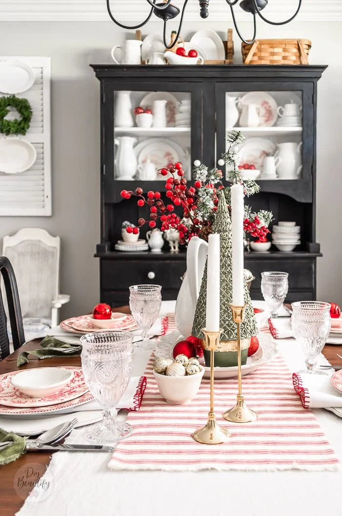 Christmas dining table with red striped runner, layered dishes and red ornaments