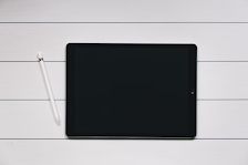 An black iPad showing the screen with a white Apple Pencil next to it.