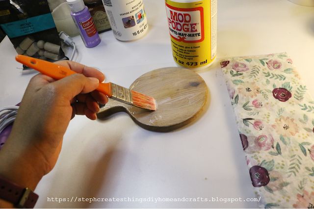 Hand holding paintbrush applying Mod Podge to round wooden board