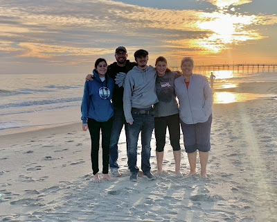 A picture of the 5 of us with the sun setting in the background over the ocean.