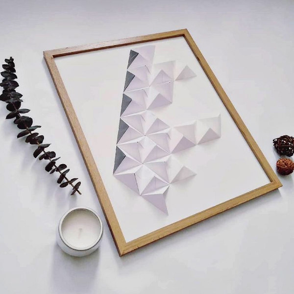 grey and white 3D modular origami wall art in light wood frame displayed on flat surface